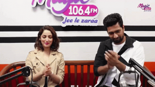 A Man And A Woman Are Clapping In Front Of A Sign That Says 106.4 Fm Jee Le Zaraa GIF