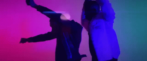 A Man And A Woman Are Dancing In A Dark Room With A Purple And Blue Light Behind Them . GIF