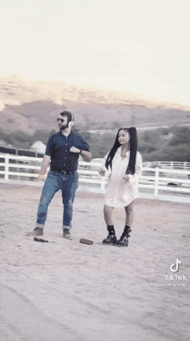 A Man And A Woman Are Dancing In A Dirt Field While Wearing Headphones . GIF