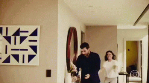 A Man And A Woman Are Dancing In A Hallway In A Living Room . GIF