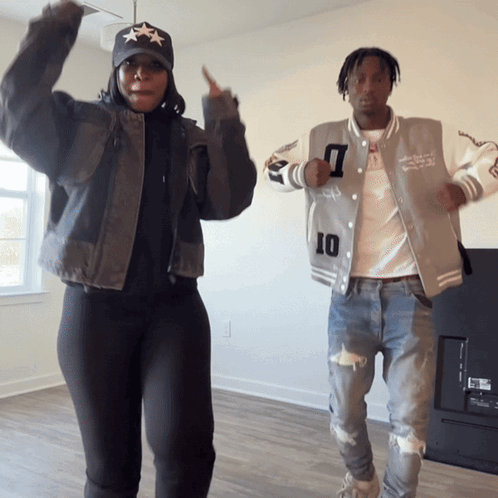 A Man And A Woman Are Dancing In A Living Room And The Man Is Wearing A Jacket With The Number 10 On It GIF