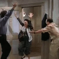 A Man And A Woman Are Dancing In A Room While A Woman Holds Her Hands Up In The Air . GIF
