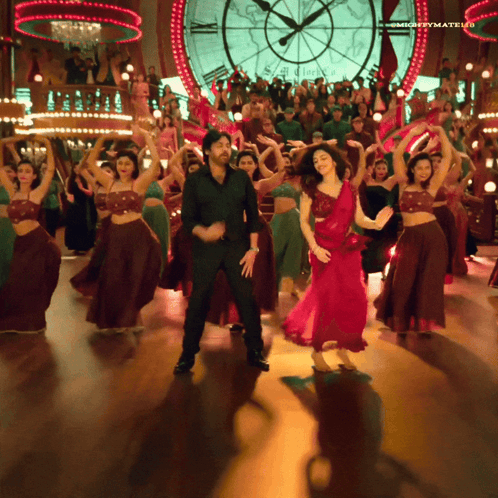 A Man And A Woman Are Dancing In Front Of A Large Clock That Says Mightymatelu GIF