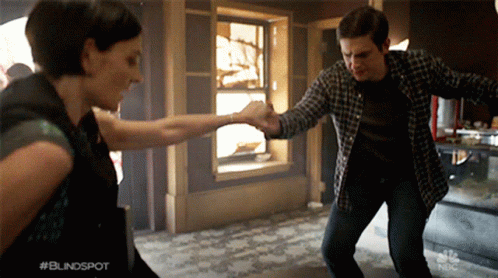 A Man And A Woman Are Dancing In Front Of A Sign That Says #Blindspot GIF