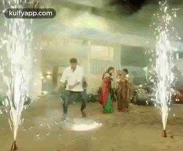 A Man And A Woman Are Dancing In Front Of Fireworks In A Parking Lot . GIF
