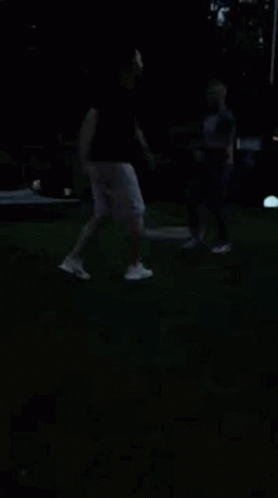 A Man And A Woman Are Dancing In The Dark On A Lush Green Field . GIF