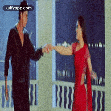 A Man And A Woman Are Dancing On A Balcony And The Woman Is Wearing A Red Dress . GIF