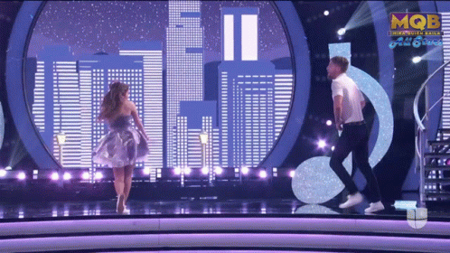 A Man And A Woman Are Dancing On A Stage With Mqbe On The Bottom Right GIF