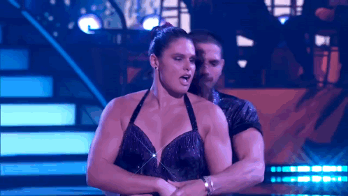 A Man And A Woman Are Dancing On A Stage With Purple Lights GIF
