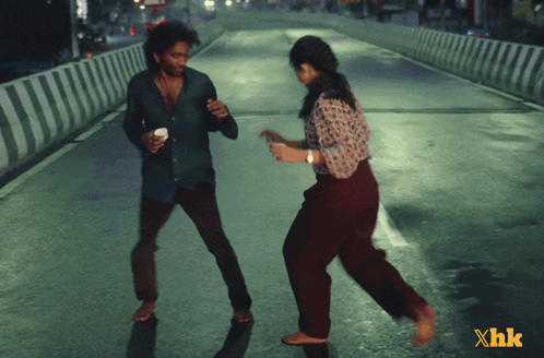 A Man And A Woman Are Dancing On A Street With Xhk Written In The Corner GIF