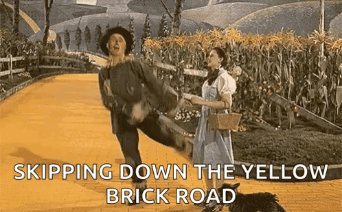 A Man And A Woman Are Dancing On A Yellow Brick Road GIF