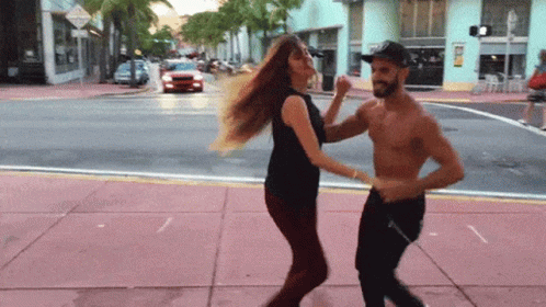 A Man And A Woman Are Dancing On The Sidewalk On A City Street GIF