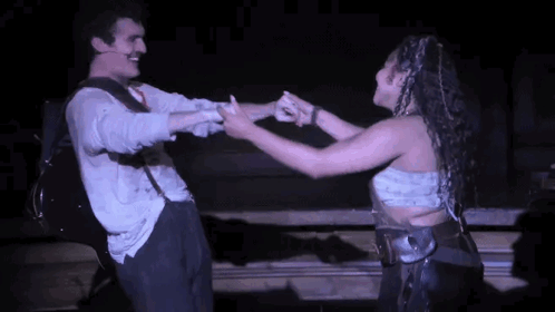 A Man And A Woman Are Dancing Together On A Stage In A Dark Room . GIF