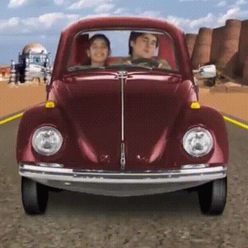 A Man And A Woman Are Driving A Red Beetle On A Road GIF
