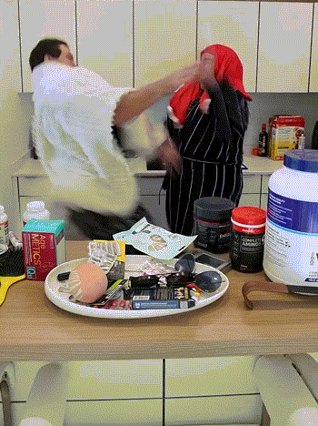A Man And A Woman Are Fighting In A Kitchen With A Bottle Of Metcalf On The Counter Top GIF