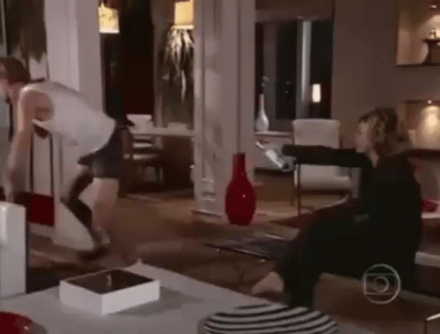 A Man And A Woman Are Fighting In A Living Room While A Woman Sits On A Couch . GIF
