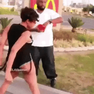 A Man And A Woman Are Fighting In Front Of A Mcdonald 'S . GIF