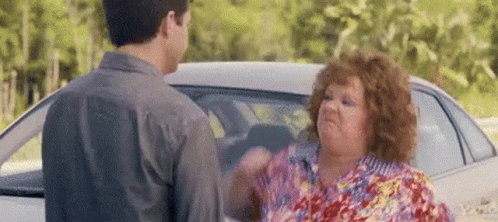 A Man And A Woman Are Having A Fight In Front Of A White Car . GIF