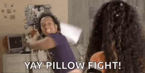 A Man And A Woman Are Having A Pillow Fight In A Room . GIF