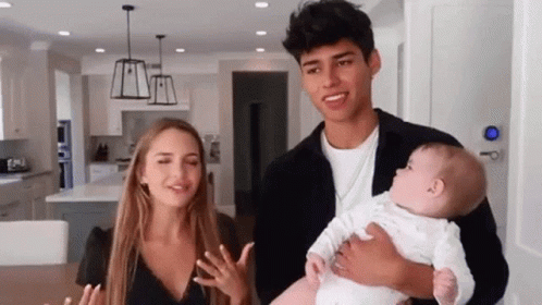 A Man And A Woman Are Holding A Baby In A Kitchen . GIF