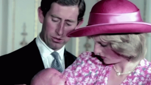 A Man And A Woman Are Holding A Baby In A Pink Hat . GIF