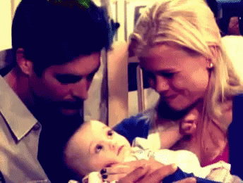 A Man And A Woman Are Holding A Baby In Their Arms GIF
