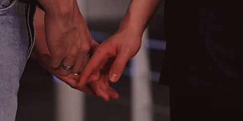 A Man And A Woman Are Holding Hands And The Woman Has A Wedding Ring On Her Finger . GIF
