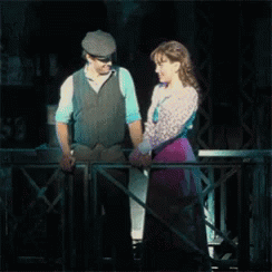 A Man And A Woman Are Holding Hands While Standing On A Balcony GIF