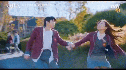 A Man And A Woman Are Holding Hands While Walking Down A Sidewalk . GIF