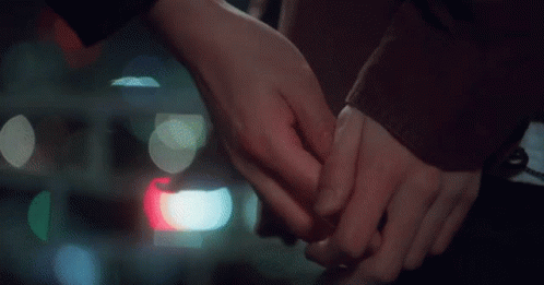 A Man And A Woman Are Holding Hands With Their Fingers Crossed . GIF