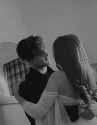 A Man And A Woman Are Hugging And Looking At Each Other In A Black And White Photo . GIF