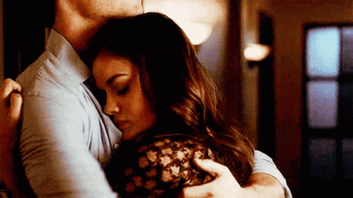 A Man And A Woman Are Hugging Each Other In A Hallway . GIF