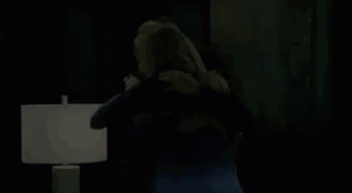 A Man And A Woman Are Hugging Each Other In A Living Room In Front Of A Lamp . GIF