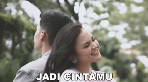 A Man And A Woman Are Hugging Each Other In A Park And The Woman Is Smiling . GIF
