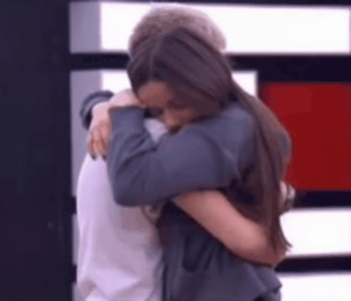 A Man And A Woman Are Hugging Each Other In Front Of A Wall . GIF