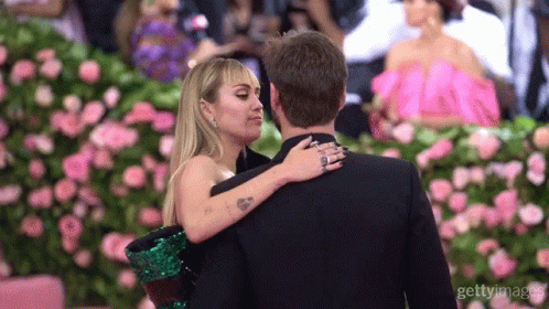 A Man And A Woman Are Hugging Each Other In Front Of Flowers GIF