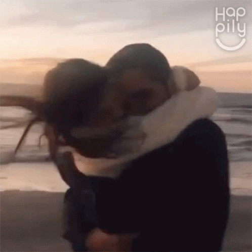 A Man And A Woman Are Hugging On A Beach . GIF