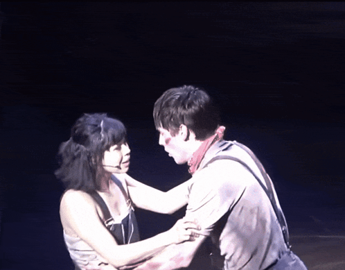 A Man And A Woman Are Hugging On A Stage In The Dark GIF