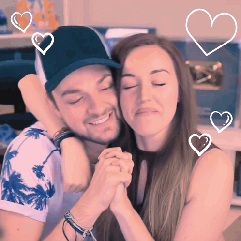 A Man And A Woman Are Hugging With Hearts Surrounding Them GIF