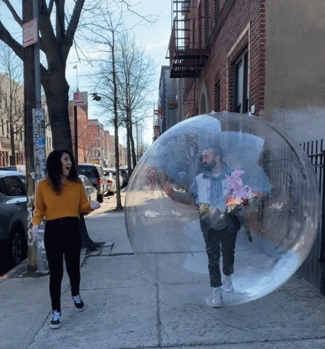 A Man And A Woman Are In A Clear Bubble On A Sidewalk GIF