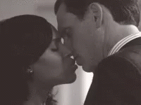 A Man And A Woman Are Kissing Each Other In A Black And White Photo . GIF
