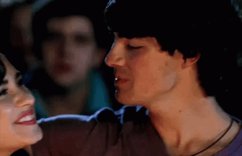 A Man And A Woman Are Kissing Each Other In A Crowded Room . GIF