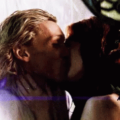 A Man And A Woman Are Kissing Each Other In A Dark Room . GIF
