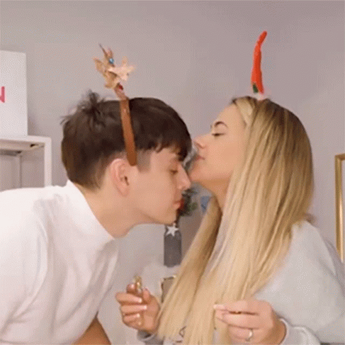 A Man And A Woman Are Kissing Each Other While Wearing Reindeer Antlers . GIF
