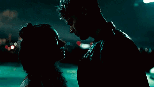 A Man And A Woman Are Kissing In A Dark Room At Night . GIF