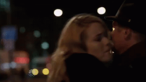 A Man And A Woman Are Kissing In A Dark Room . The Woman Is Wearing A Hat . GIF