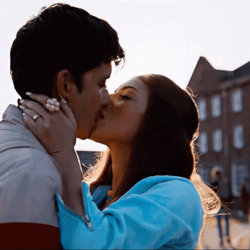 A Man And A Woman Are Kissing In Front Of A Brick Building GIF