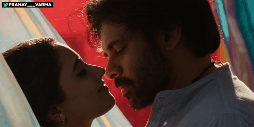A Man And A Woman Are Kissing In Front Of A Sign That Says Pranay Varma GIF