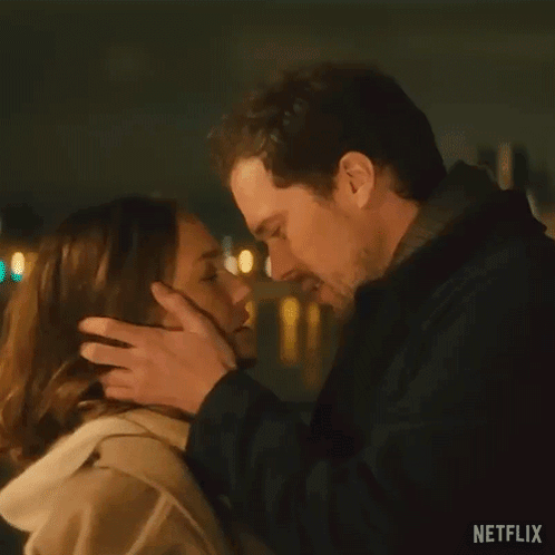 A Man And A Woman Are Kissing In Front Of A Street Light At Night . GIF