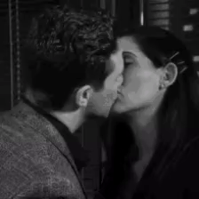 A Man And A Woman Are Kissing In Front Of A Window In A Black And White Photo . GIF